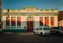 Fachada colorida de um prédio de prefeitura, com pessoas circulando em frente ao edifício.