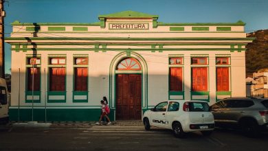 Fachada colorida de um prédio de prefeitura, com pessoas circulando em frente ao edifício.