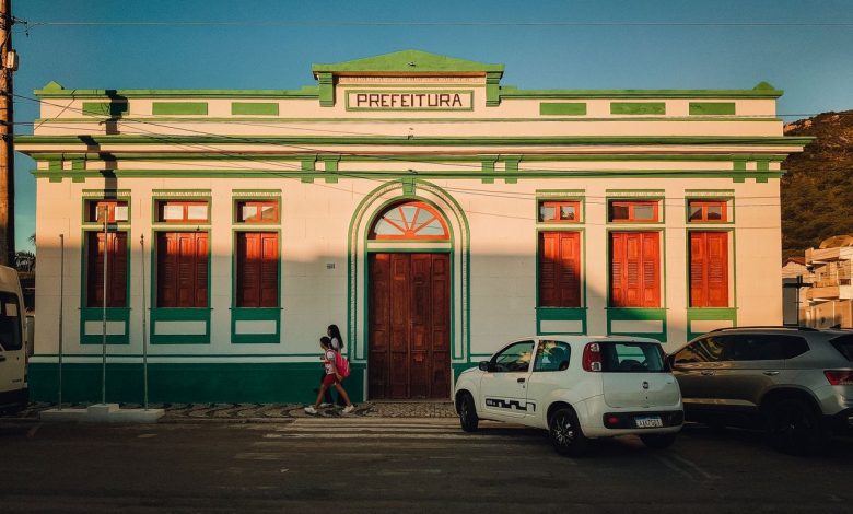 Fachada colorida de um prédio de prefeitura, com pessoas circulando em frente ao edifício.